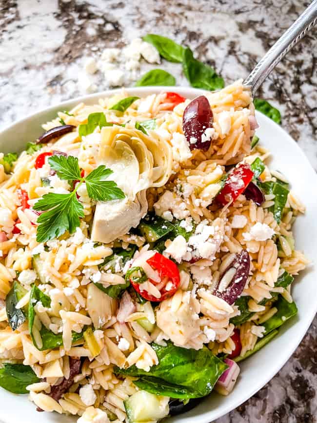 A spoon digging into a bowl of Greek Orzo Salad