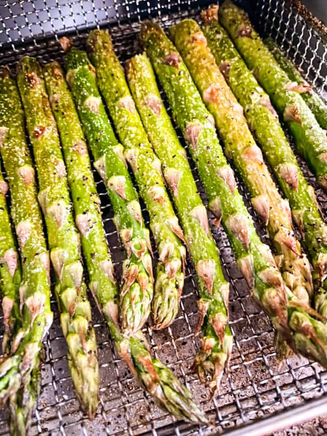 Asparagus stalks coming out of an air fryer machine in a basket