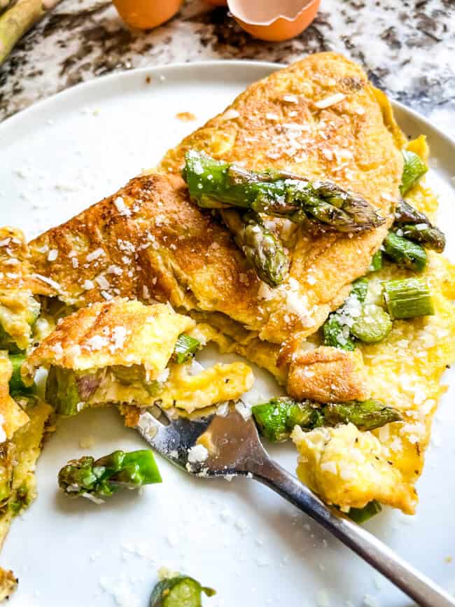 A fork with half eaten Asparagus Omelette on a white plate