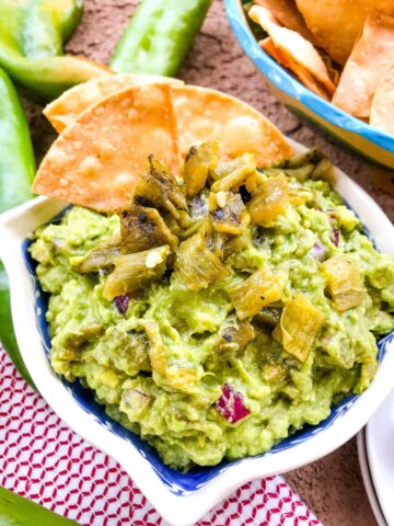 A bowl of Hatch Green Chile Guacamole with some chips sticking out of it