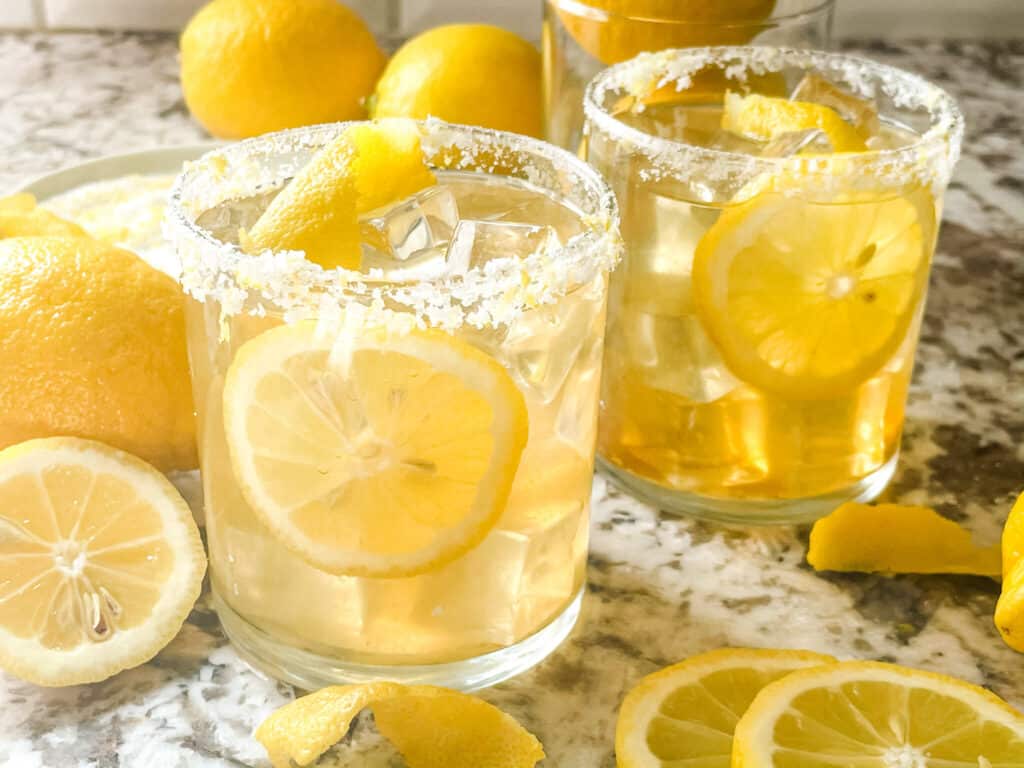 Two cocktails with salt rims and citrus around them