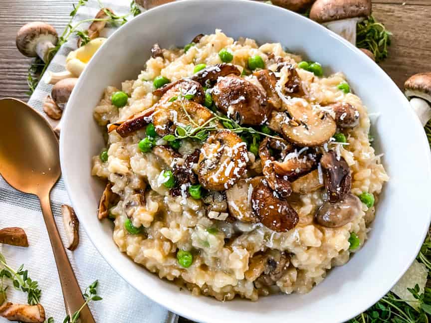 A white bowl full of Mushroom Pea Risotto with a spoon next to it