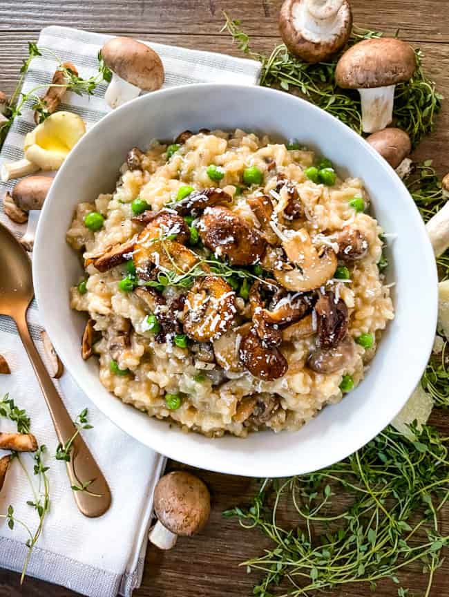 The Italian rice in a white bowl with thyme and mushrooms around it