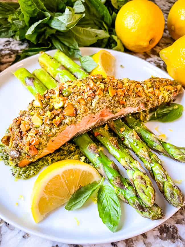 Crusted fish on a bed of air fryer asparagus on a white plate with lemons