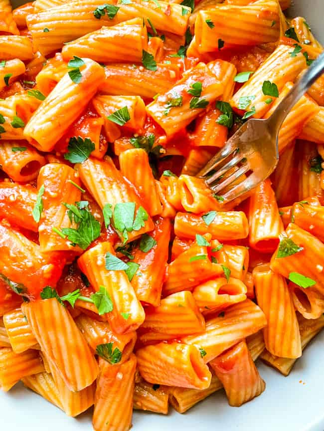 A fork digging into a large bowl of Rigatoni Arrabbiata