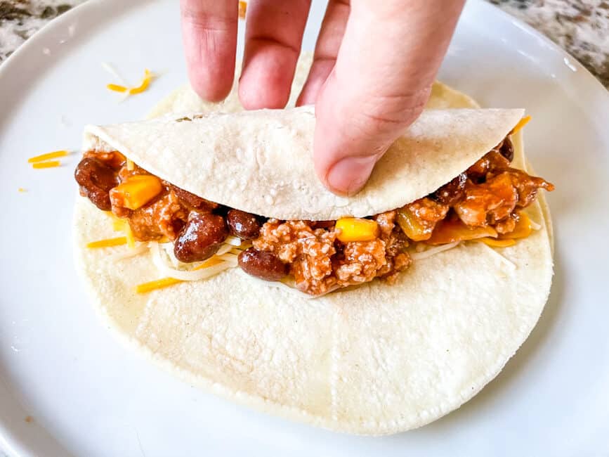 A hand rolling a tortilla with the filling