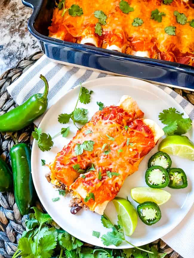Southwest Ground Turkey Enchiladas on a plate with the rest in a dish nearby. Limes and jalapenos around the dish.