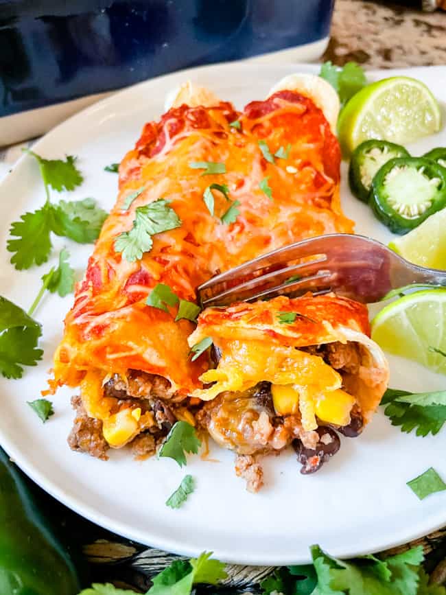 A fork cutting into an enchilada on a plate