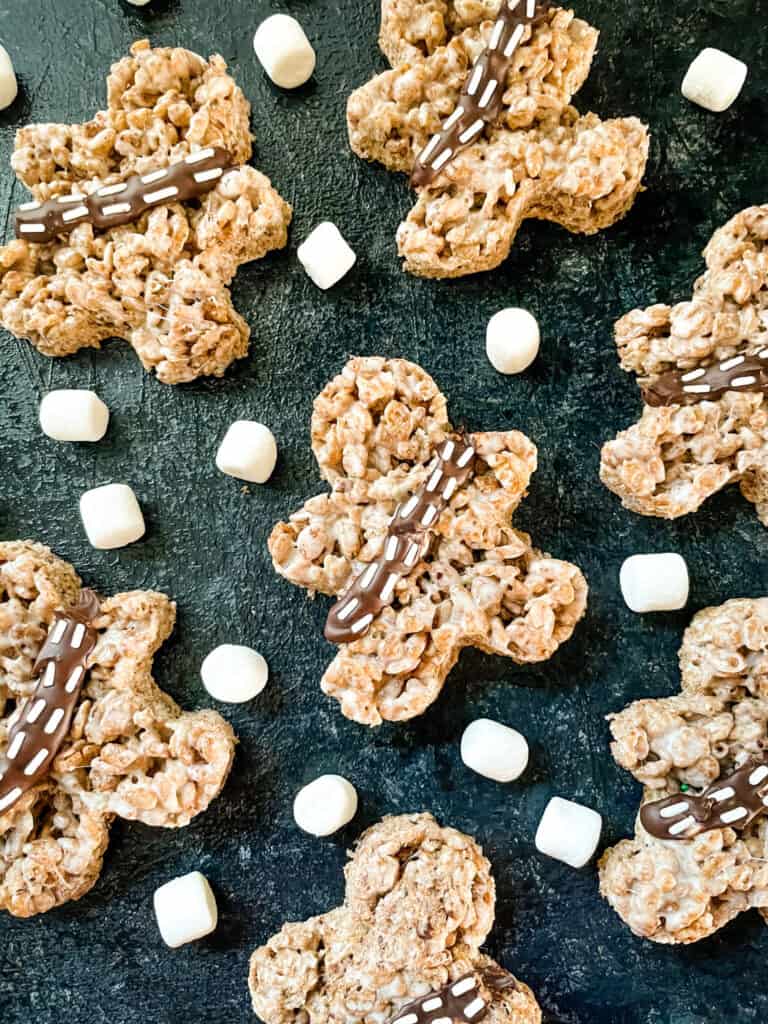 Several person shaped treats on a black board with marshmallows