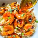 A spoon pouring sauce over Chipotle Orange Glazed Shrimp on top of noodles