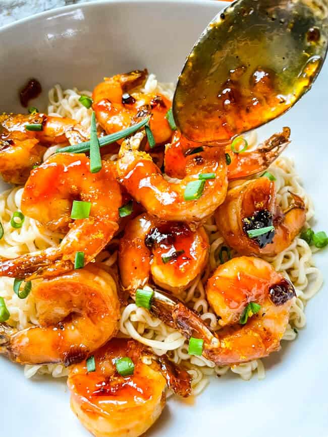 A spoon pouring sauce over Chipotle Orange Glazed Shrimp on top of noodles