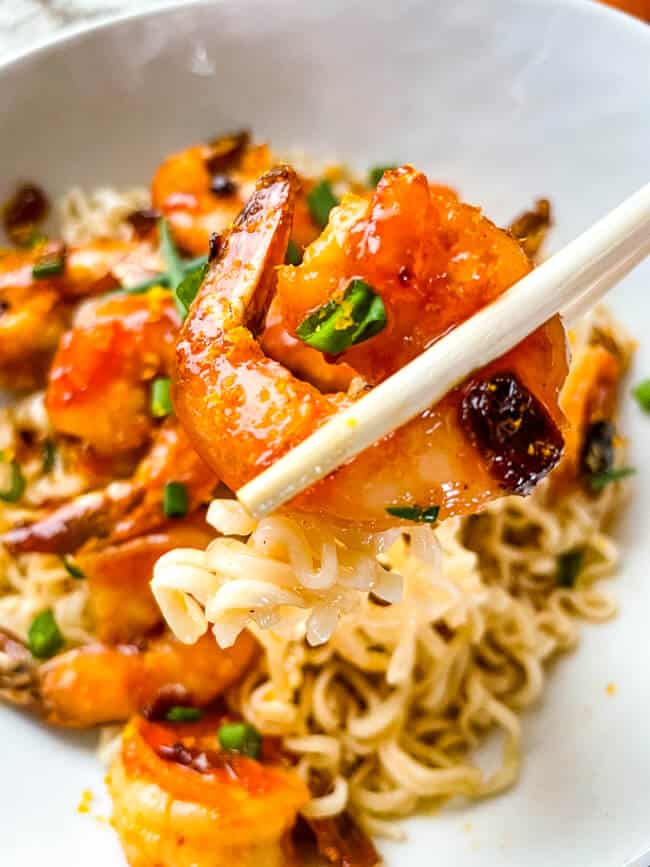 Chopsticks holding a shrimp over a bowl of the food