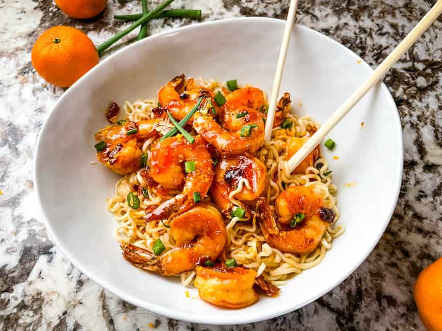 A white bowl with noodles and the seafood. Chopsticks sticking out of the bowl