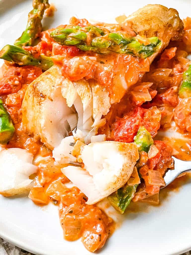 A Cod Pomodoro with Asparagus with a fork having dug into the flaky fish