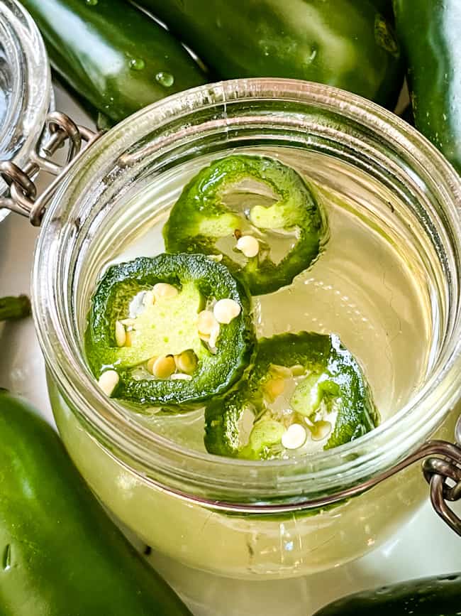 Sliced peppers and the sugar syrup in a jar