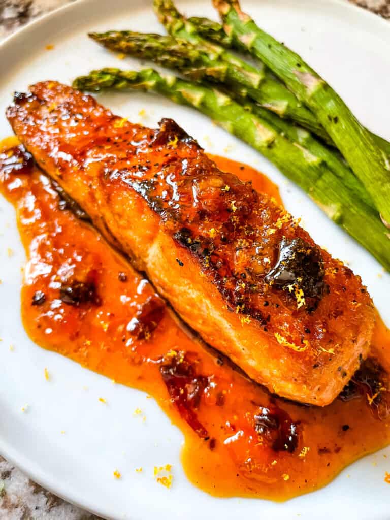 A full Chipotle Orange Glazed Salmon steak with sauce on a white plate with asparagus