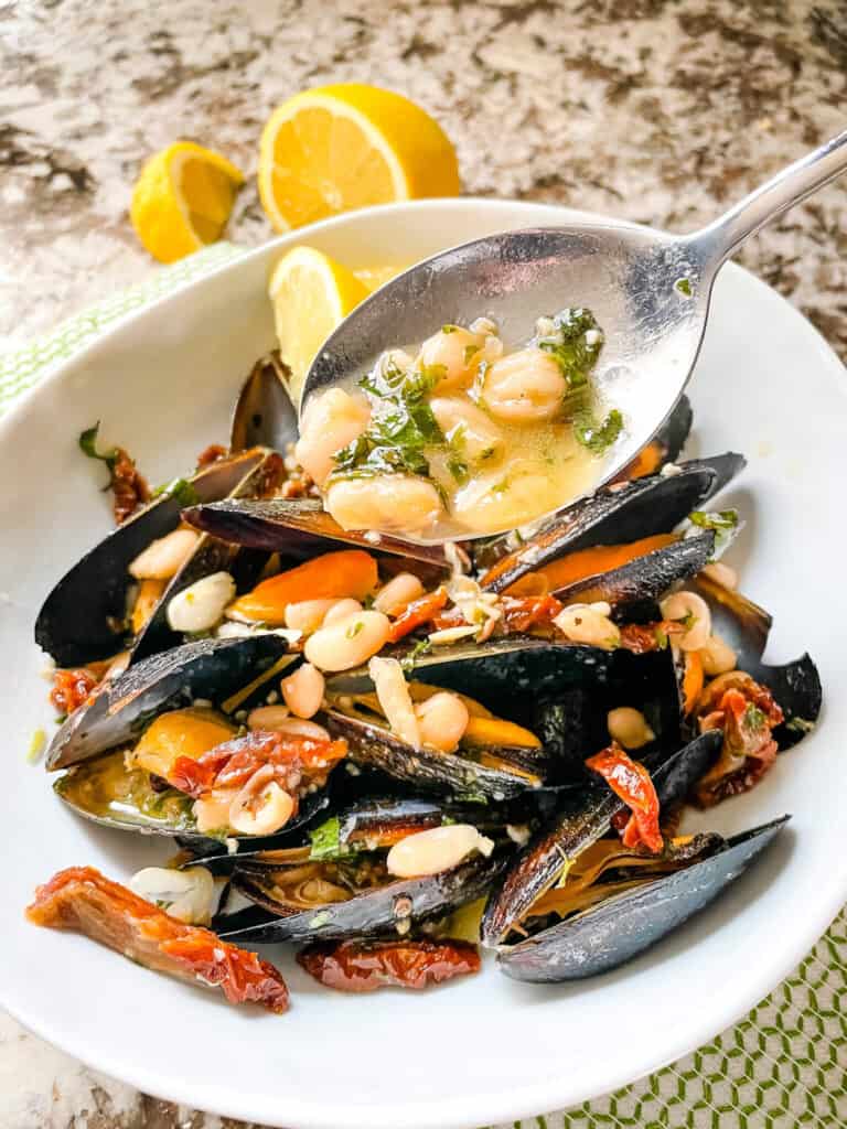 A spoon scooping the bean sauce mixture onto the shellfish