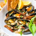 Copycat Maggiano's Tuscan Mussels in a white bowl with lemons and bread