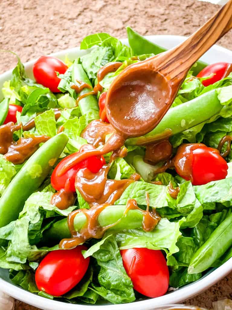 A wood spoon pouring Creamy Balsamic Dressing on a salad