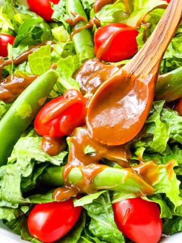 A wood spoon with some dressing on it resting in a dressed salad