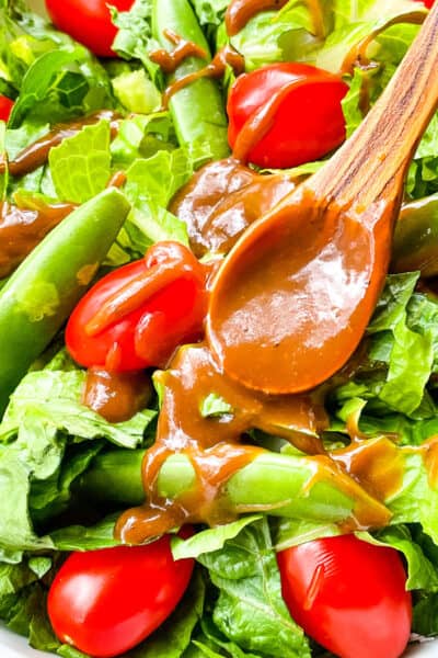 A wood spoon with some dressing on it resting in a dressed salad