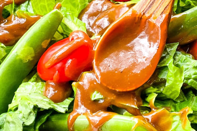 A wood spoon with some dressing on it resting in a dressed salad