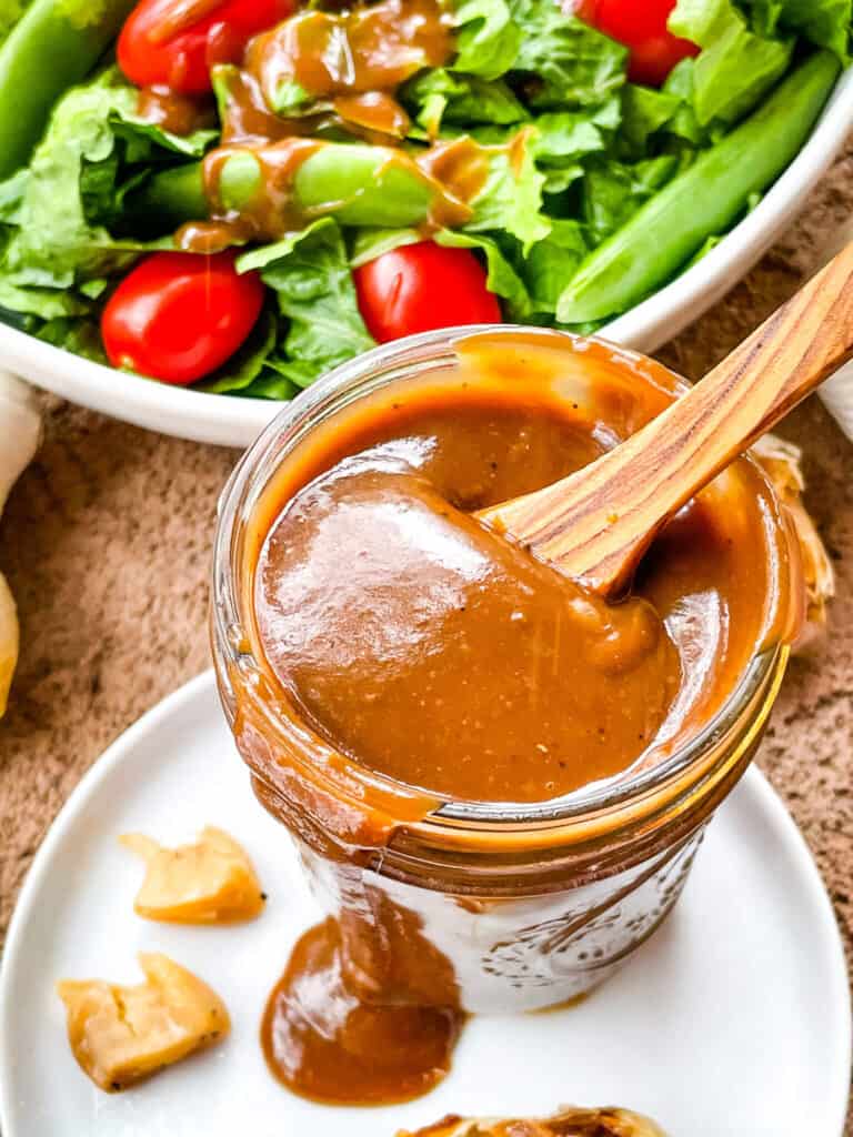 A jar of Creamy Balsamic Dressing with a wood spoon sticking out
