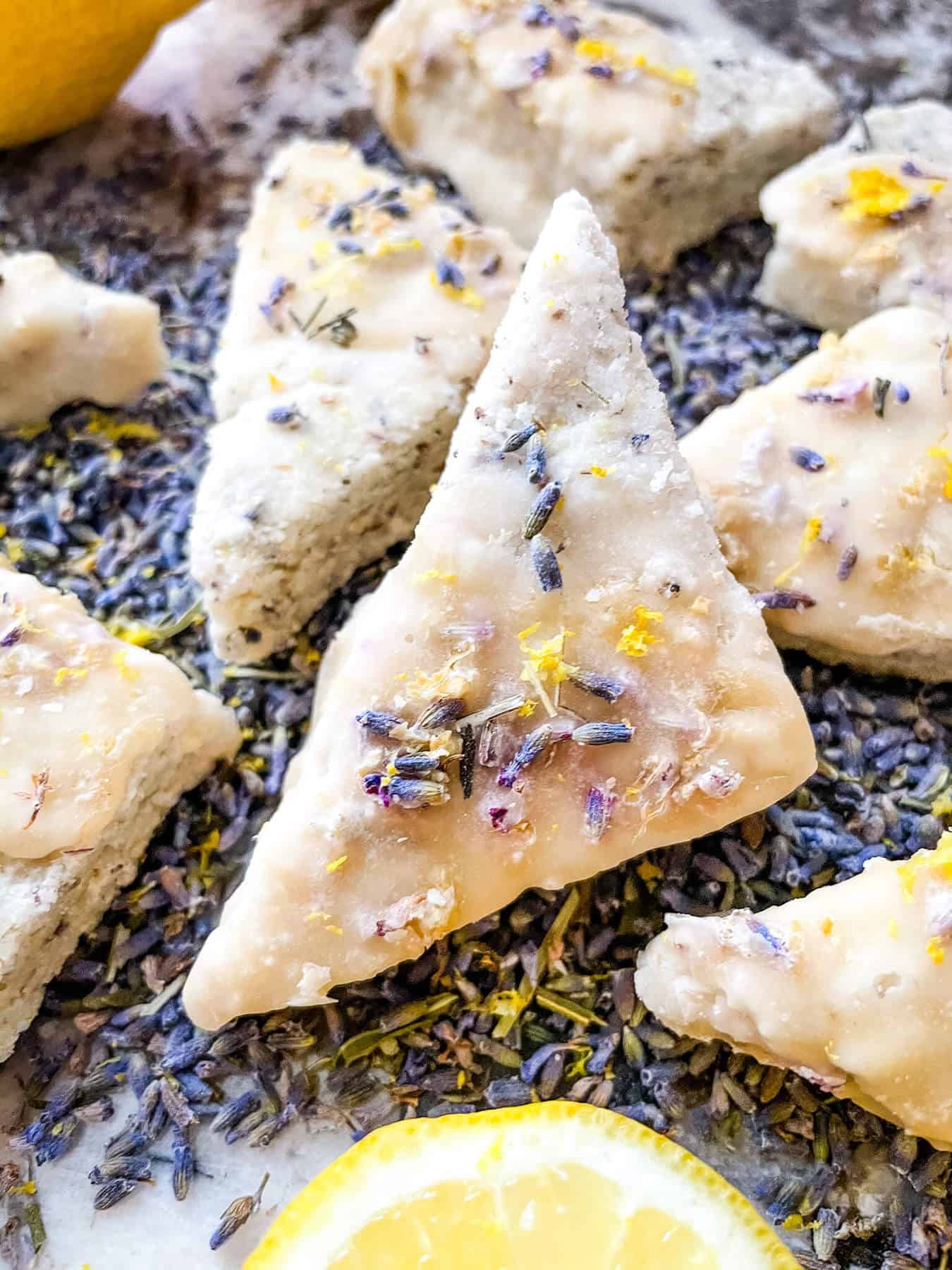 A close up of a triangular lavender cookie on top of flowers