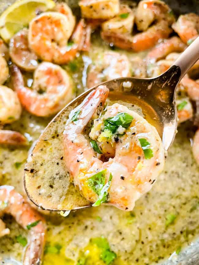 A copper spoon scooping a shrimp and sauce out of the pan