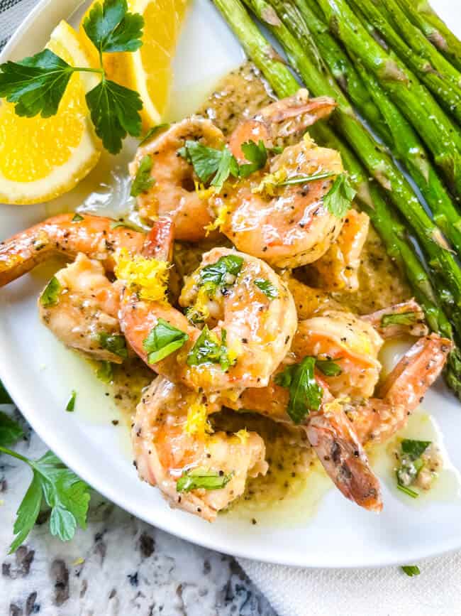 Lemon Pepper Shrimp piled on a white plate next to asparagus