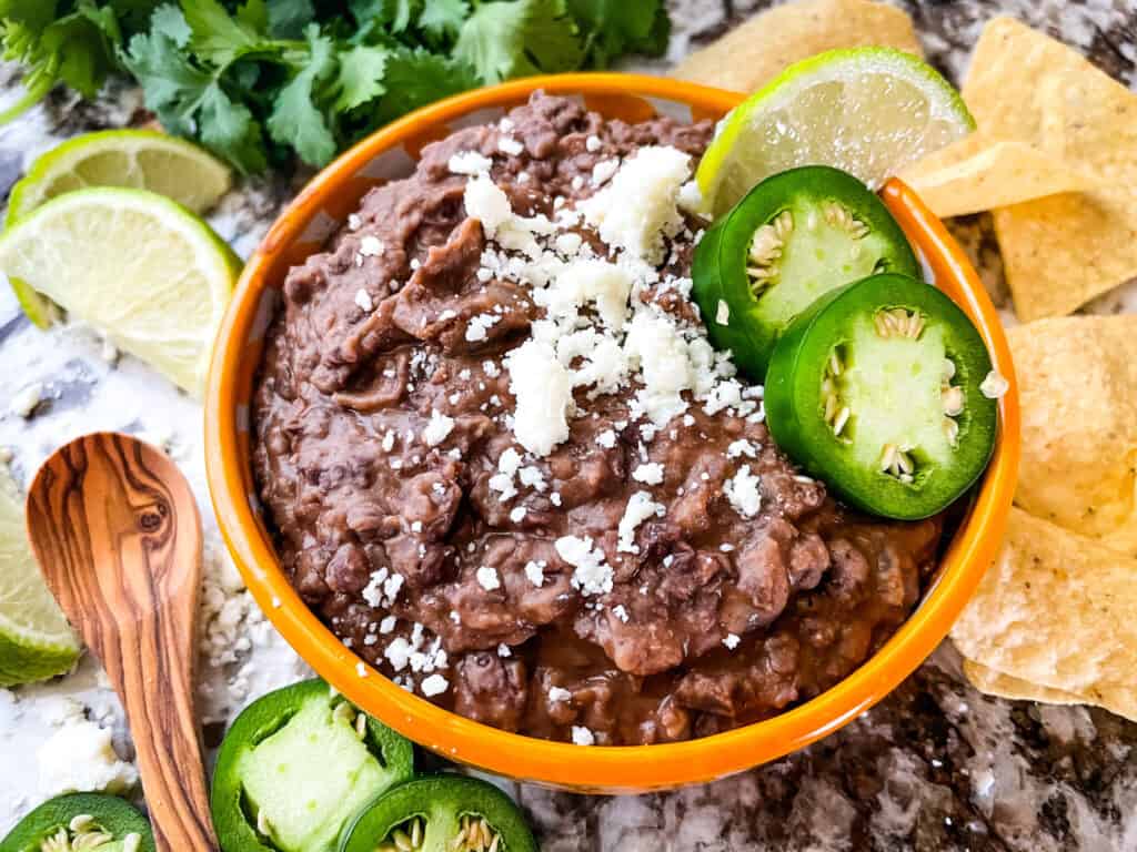 The beans in a yellow bowl with chips and limes around it