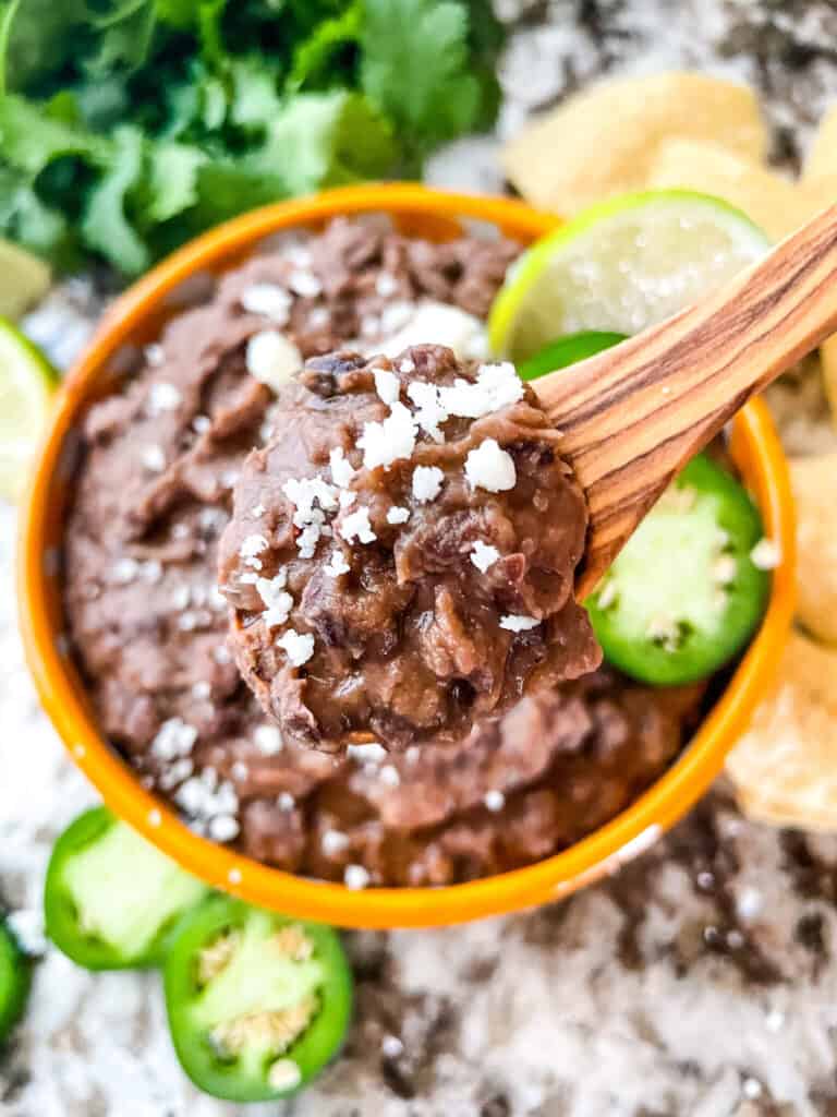 Black Refried Beans on a wood spoon hovering over the bowl