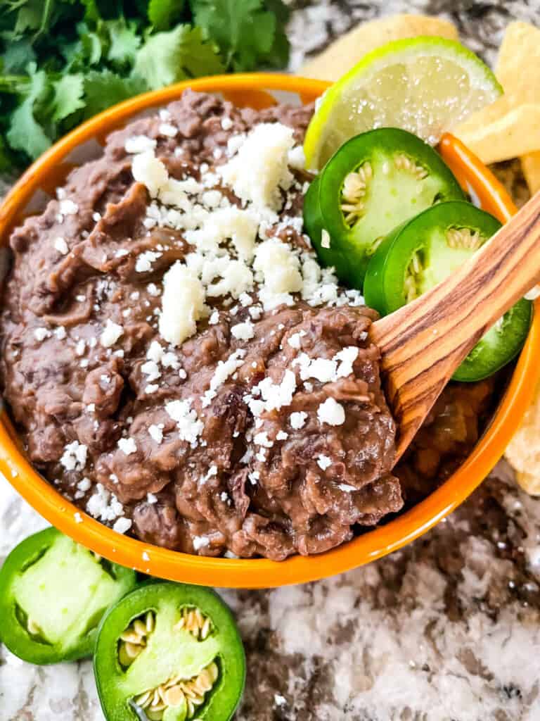 A spoon digging into a yellow bowl of Black Refried Beans