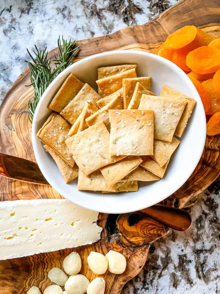 A white bowl full of Rosemary Sourdough Crackers on a charcuterie board