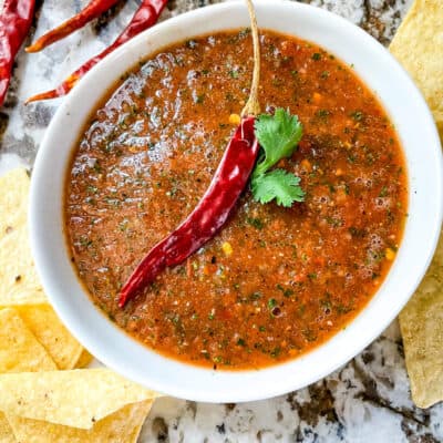 The salsa in a white bowl with a pepper and chips around it