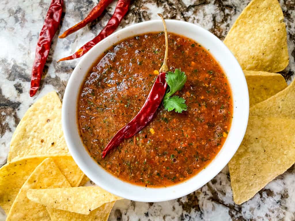 A white bowl full of Salsa Chile de Arbol with a pepper on top