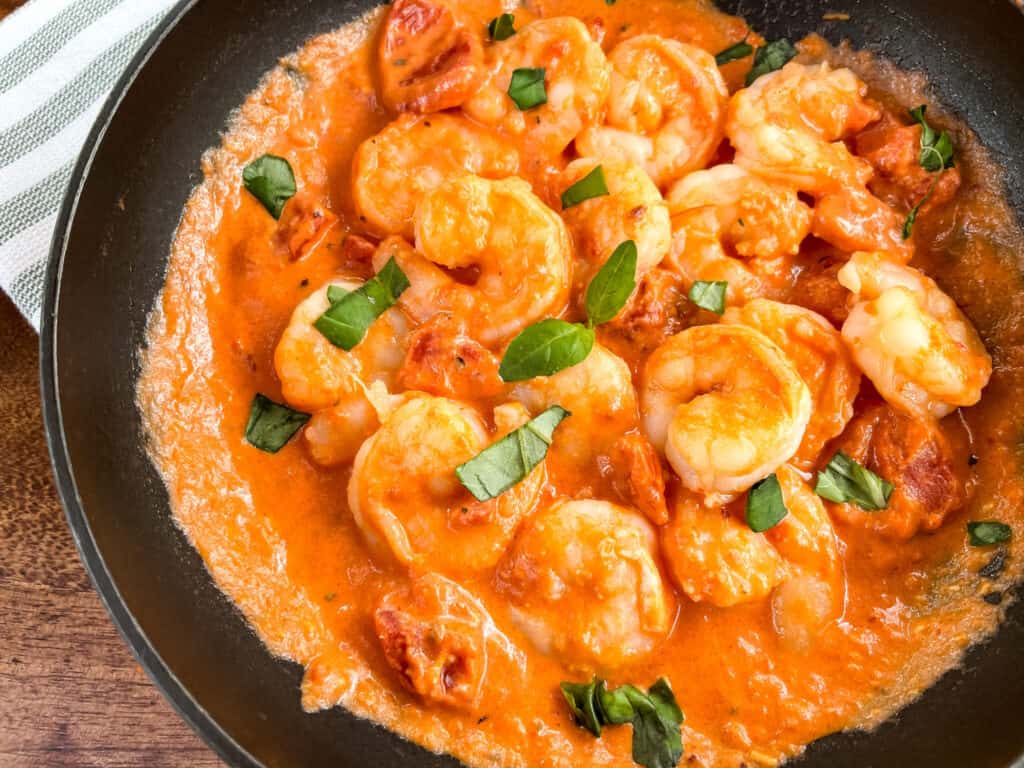 Closer view of Shrimp in Vodka Sauce in a black skillet with pieces of basil on top
