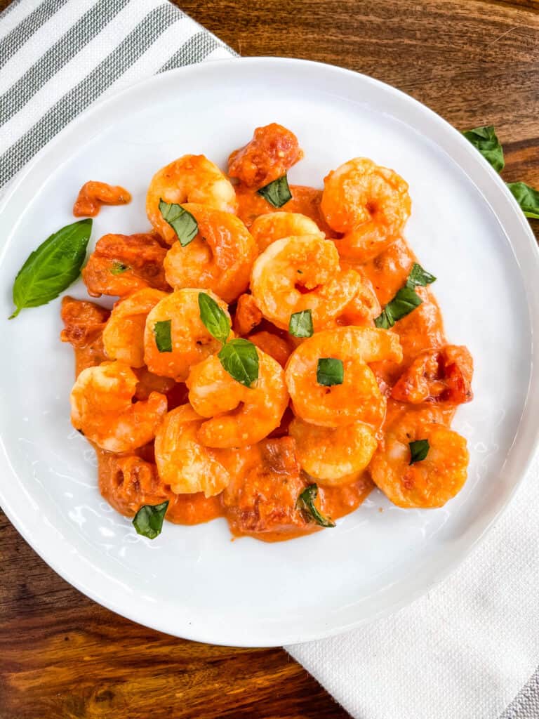 Top view of a pile of Shrimp in Vodka Sauce on a white plate with pieces of fresh basil