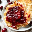 Cranberry Jam on an English muffin on a plate with some berries around it