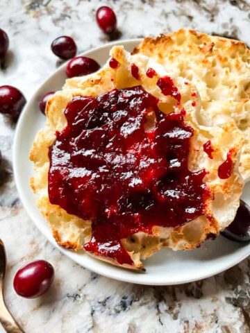 Cranberry Jam on an English muffin on a plate with some berries around it