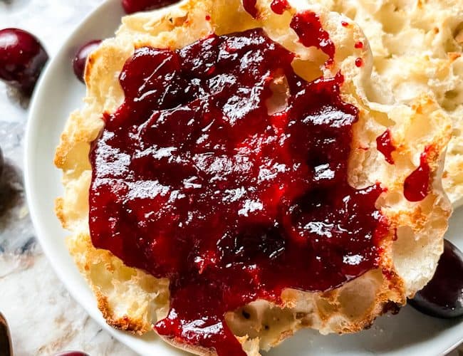 Cranberry Jam on an English muffin on a plate with some berries around it