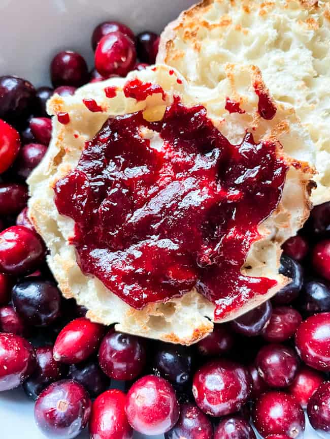 Cranberry Jam on an English muffin sitting in a bowl full of fresh cranberries