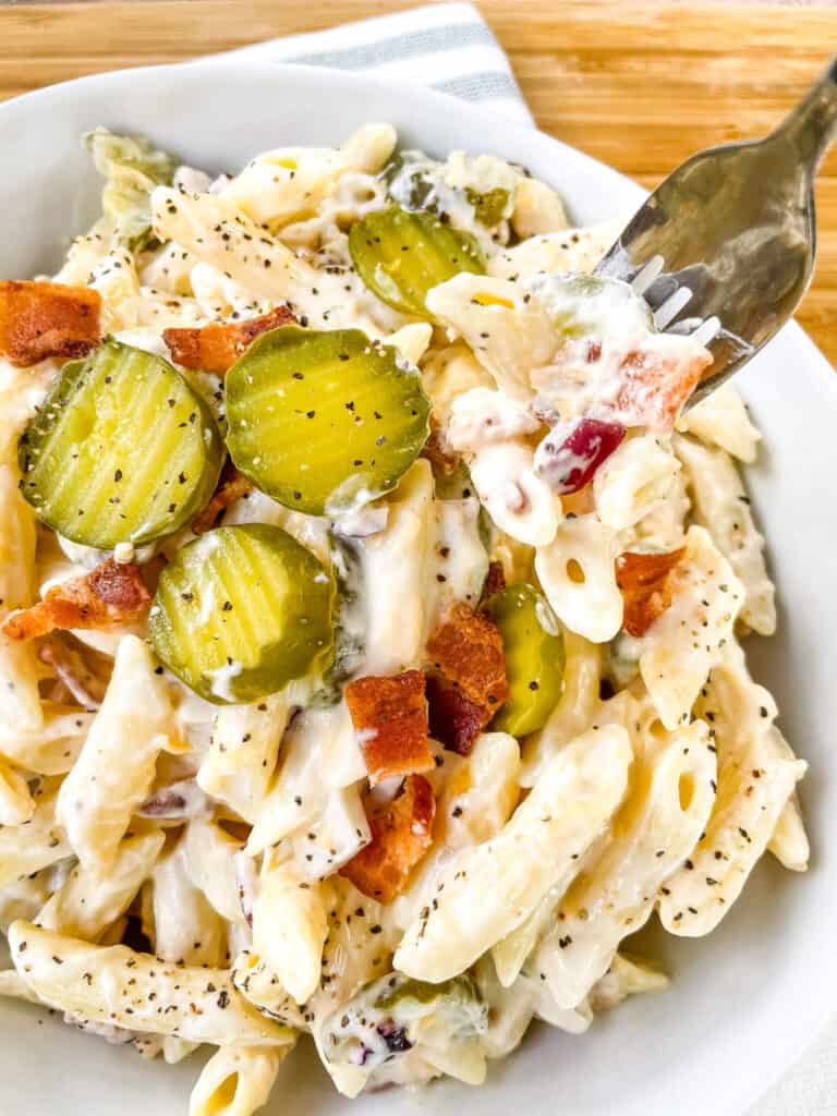 A fork digging into a bowl of Dill Pickle Pasta Salad with Bacon