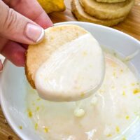 A hand dunking a lemon shortbread into lemon glaze