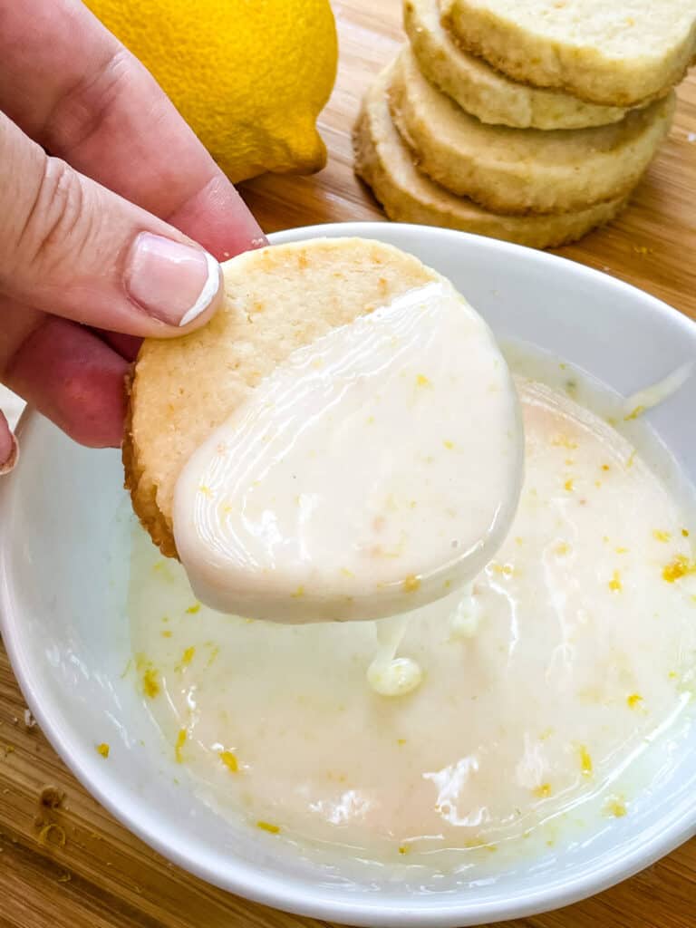 A hand dunking a lemon shortbread into lemon glaze