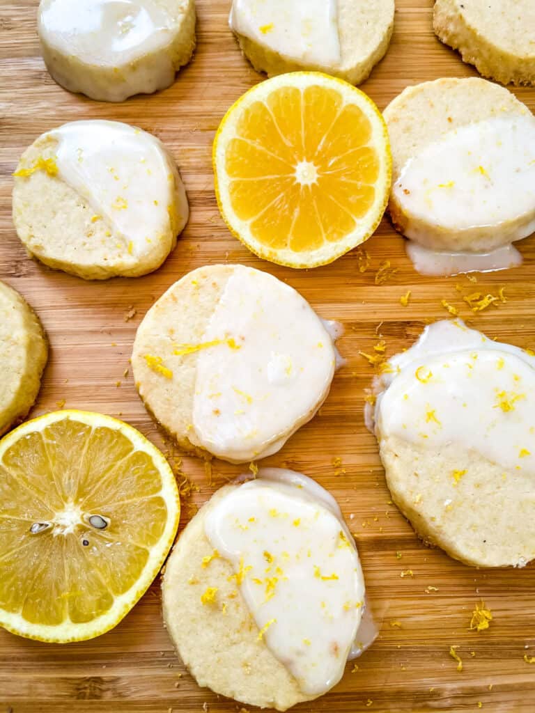 Cookies dipped in glaze spread out on a cutting board with lemon wheels