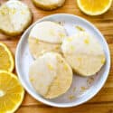 A white round plate with three Lemon Shortbread dipped in glaze surrounded by lemon slices and more cookies