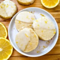 A white round plate with three Lemon Shortbread dipped in glaze surrounded by lemon slices and more cookies