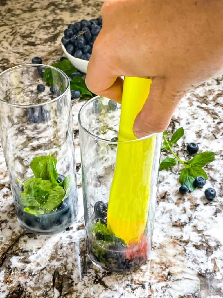 A hand muddling ingredients in a tall glass