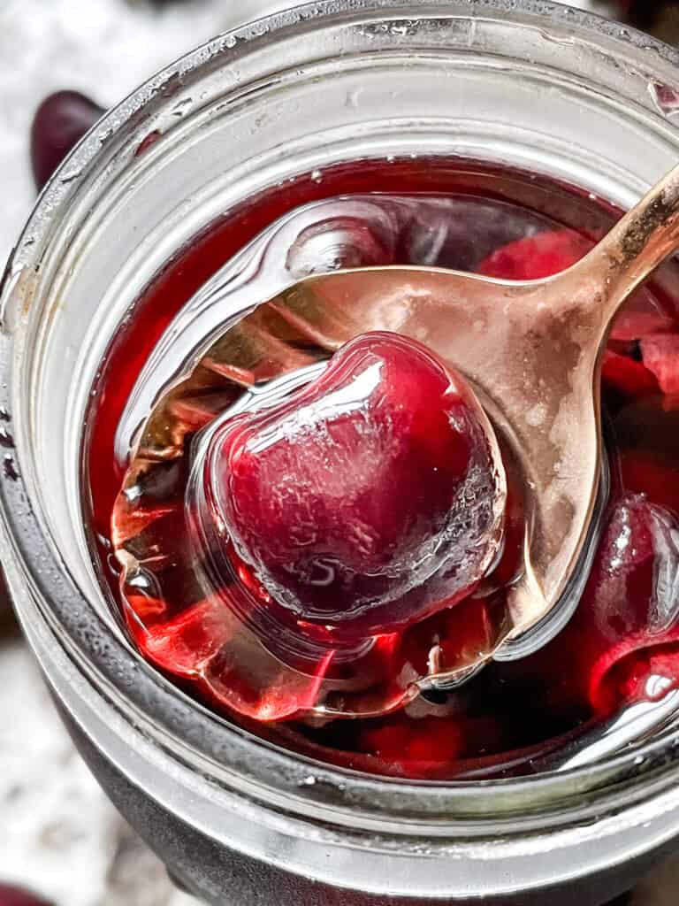 A spoon scooping a cherry out of the jar